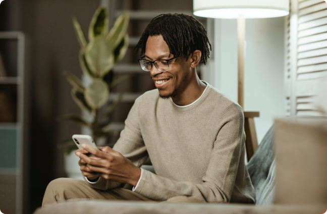 Homem negro com moletom bege mexendo no celular e sorrindo.